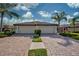 Two-car garage with a brick driveway and tropical landscaping at 20272 Tesoro Dr, Venice, FL 34293