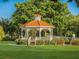 White gazebo with orange roof tiles, surrounded by lush green grass, trees and benches at 12198 Wakulla Pl, Venice, FL 34293