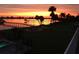 Tranquil waterfront view during sunset, featuring a dock, a sandy firepit area, and palms at 1784 Bayshore Dr, Englewood, FL 34223