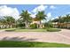 Attractive community entrance with a circular driveway, lush landscaping, and palm trees under a partly cloudy sky at 20590 Granlago Dr, Venice, FL 34293