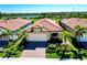 Aerial view of a home with a red tile roof, brick driveway, and lush landscaping near a serene lake at 24229 Spartina Dr, Venice, FL 34293