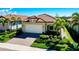 Well-maintained single-story home with a red tile roof, brick driveway, and tropical palm trees at 24229 Spartina Dr, Venice, FL 34293