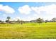 Scenic golf course view with lush green grass, a serene pond, and golf carts under a sunny, partly cloudy sky at 734 Brightside Crescent Dr # 18, Venice, FL 34293