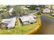 Aerial view of a lakeside home with a screened lanai, lush landscaping, and a neutral colored roof at 803 Carnoustie Dr, Venice, FL 34293