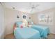 Bright bedroom featuring twin beds with blue bedding, ceiling fan, and window with plantation shutters at 803 Carnoustie Dr, Venice, FL 34293
