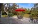 Outdoor patio featuring a black grill and outdoor furniture with a red umbrella for shade, surrounded by lush greenery at 2537 Northway Dr, Venice, FL 34292