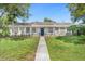 Charming home featuring a brick façade porch, blue door, and a well-manicured front yard with mature trees at 1390 Eastfield Dr, Clearwater, FL 33764