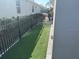 Narrow side yard covered in artificial turf and enclosed by a black metal fence at 11400 Burgundy Dr, Venice, FL 34293