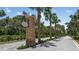 Beautiful stone community entrance sign with manicured landscaping and towering palm trees along the drive at 23819 Collina Way # 011101, Port Charlotte, FL 33980