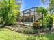 Landscaped backyard featuring a screened-in pool area with lush greenery and a well-manicured lawn at 7656 Portstewart Dr, Lakewood Ranch, FL 34202