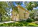 Side view of a yellow three-story home featuring a three-car garage, lush landscaping, and mature trees at 6231 Bayshore Blvd, Tampa, FL 33611