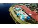 Aerial view of a community pool with palm trees, lounge chairs and seating areas, adjacent to a lake at 5011 Sandy Brook Cir, Wimauma, FL 33598