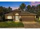 Evening view of a tan one-story house with a two-car garage and landscaped lawn at 4275 Caskie Pl, Brooksville, FL 34604