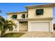 Two-story house with a yellow facade, white garage doors, and palm trees at 11325 5Th E St, Treasure Island, FL 33706