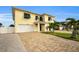 Two-story house with a yellow facade, white garage doors, and palm trees at 11325 5Th E St, Treasure Island, FL 33706