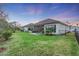 Home's backyard features a screened patio, grassy lawn, and a privacy fence at dusk at 5225 Caserta Ct, Palmetto, FL 34221