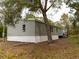 Gray mobile home with white skirting, situated on a lot with leaf-covered ground at 12816 Midvale Ave, New Port Richey, FL 34654