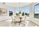 Sunlit dining area with a round table, six white chairs, and large windows overlooking a green landscape at 5214 Lake Venice Dr, Wimauma, FL 33598