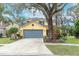 Two-story yellow house with gray garage door, landscaping, and a large tree in the front yard at 5608 Rockfield Loop, Valrico, FL 33596