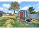 Gray shed with red door in landscaped backyard setting at 11201 Lake Sassa Dr, Thonotosassa, FL 33592