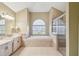 Primary bathroom featuring double vanity, a large tub under an arched window, and tiled shower at 4534 Cozzo Dr, Land O Lakes, FL 34639