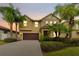 Two story house with tan exterior, brown garage door, and palm trees at dusk at 19231 Pepper Grass Dr, Tampa, FL 33647