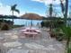 Peaceful waterfront patio with pink table and chairs,thatched umbrella, and lush landscaping at 7127 Peninsular Dr, New Port Richey, FL 34652