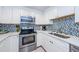 Modern kitchen with white cabinets, stainless steel appliances, and mosaic backsplash at 2700 Bayshore Blvd # 11302, Dunedin, FL 34698