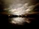 Night view of the lake, with a reflection of the clouds and lights on the water and silhouettes of trees and houses at 17014 Clear Cork Dr, Wimauma, FL 33598