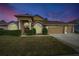 Evening view of tan house with three-car garage and landscaping at 10025 Cypress Shadow Ave, Tampa, FL 33647