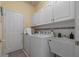 Bright laundry room featuring white cabinets, appliances, and a convenient utility sink at 15555 Martinmeadow Dr, Lithia, FL 33547