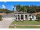 White house with dark brown roof, 3-car garage, and lush landscaping at 1257 Kings Way Ln, Tarpon Springs, FL 34688