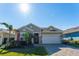 Tan house with red accents, a two-car garage, and lush landscaping at 14015 Kingfisher Glen Dr, Lithia, FL 33547