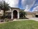 Tan house with a red door, three-car garage, and lush landscaping at 3011 Marble Crest Dr, Land O Lakes, FL 34638