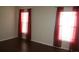 Bedroom featuring wood-look flooring, neutral walls, and two windows dressed with translucent red curtains at 5532 War Admiral Dr, Wesley Chapel, FL 33544