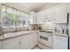 Bright kitchen features white cabinets, beige countertops, and double bowl sink under a window with tropical print curtains at 4210 Revere Cir, New Port Richey, FL 34653