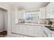 Bright kitchen features white cabinets, beige countertops, and double bowl sink under a window with tropical print curtains at 4210 Revere Cir, New Port Richey, FL 34653