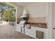 Outdoor kitchen featuring a stainless steel grill, sink, and tile backsplash on a brick paver patio at 7401 Watersilk Dr, Pinellas Park, FL 33782