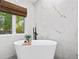 Modern bathroom with marble walls, a freestanding tub, and a window offering natural light and green views at 2186 Coffee Pot Ne Blvd, St Petersburg, FL 33704