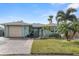 Charming single-story home featuring a well-manicured lawn, palm trees, and a brick-paved driveway leading to an attached garage at 6702 Harbor Dr, Hudson, FL 34667