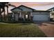Inviting single-story home with a well-kept lawn, brick driveway, and welcoming front porch at dusk at 18863 Roseate Dr, Lutz, FL 33558
