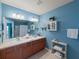 Bright blue bathroom featuring double sinks, a large mirror, and decorative storage shelves at 10120 Post Harvest Dr, Riverview, FL 33578