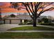 Charming single-story home with a three-car garage, mature landscaping, and a vibrant sunset backdrop at 16908 Equestrian Trl, Odessa, FL 33556