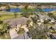 An aerial view shows a tan home with a manicured lawn next to a blue lake in a golf course community at 2471 Kensington Greens Dr, Sun City Center, FL 33573