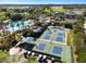 Aerial view featuring a community pool and tennis courts, surrounded by lush greenery and towering palm trees at 2471 Kensington Greens Dr, Sun City Center, FL 33573