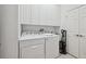 Well-lit laundry room with white washer, dryer, cabinets, utility sink and convenient vacuum storage at 2471 Kensington Greens Dr, Sun City Center, FL 33573