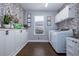 Well-lit laundry room with floral wallpaper, white cabinets, and modern appliances at 5292 Kernwood Ct, Palm Harbor, FL 34685