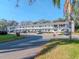 Exterior view of white, two-story apartment complex with balconies, parking, and mature trees in the background at 300 Glennes Ln # 208, Dunedin, FL 34698