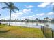 Waterfront backyard with green grass, tropical foliage, and a chain link fence on a sunny day at 3832 Star Island Dr, Holiday, FL 34691