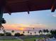 Sunset water view framed by palm trees, viewed from a covered balcony, with a glimpse of nearby street and walkway at 620 Scotland St, Dunedin, FL 34698